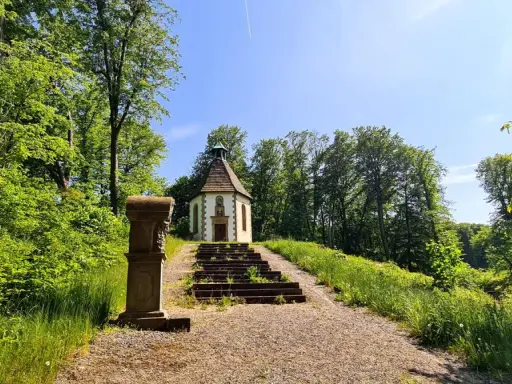 Ein kleiner Weg führt zu einer Kapelle auf einem Hügel, umgeben von grünen Bäumen. Der schmetterlingspfad willebadessen lädt zum Entdecken ein.