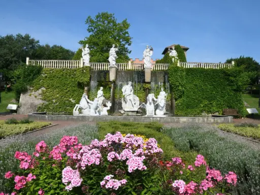 Prachtvoller Brunnen mit Skulpturen und Wasserfällen, umgeben von blühenden Blumen und Grün im botanischen Garten NRW.