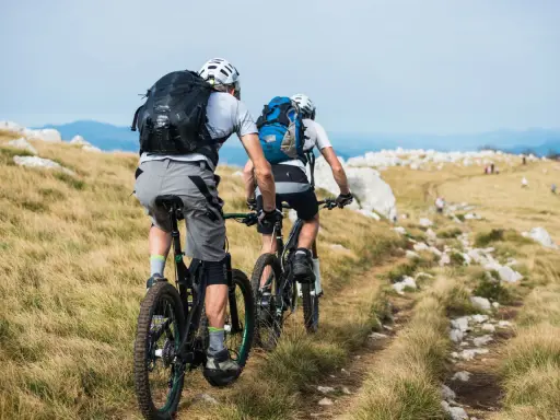 Zwei Radfahrer mit Rucksäcken auf einem Bergpfad. Perfekt für Radreisen und Sternfahrten in der Natur.