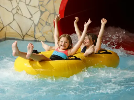 Zwei lachende Kinder rutschen auf einem gelben Schlauchboot durch einen Wasserpark. Ein perfekter Tag, wie ein h2o gutschein!