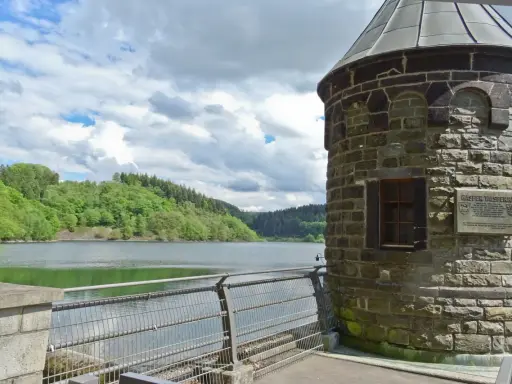 Ein schöner Tag zum spazieren gehen am NRW See. Ein alter Turm steht am Ufer, umgeben von grünen Hügeln und einem ruhigen See.