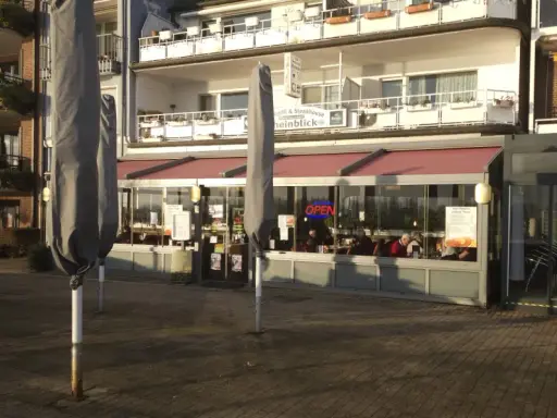 Geschlossene Sonnenschirme säumen die rheinpromenade emmerich. Ein Restaurant mit "OPEN"-Schild lädt zum Verweilen ein.