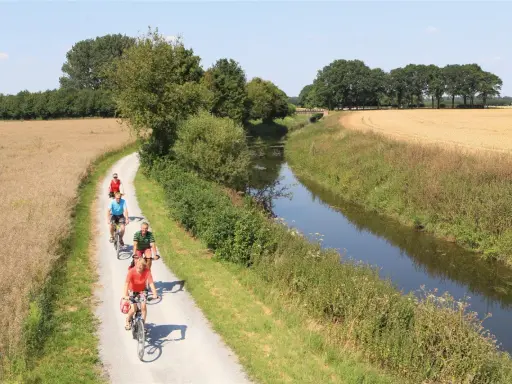 Radfahrer genießen die Fahrt auf dem werse ems radweg entlang eines Kanals und durch Felder.