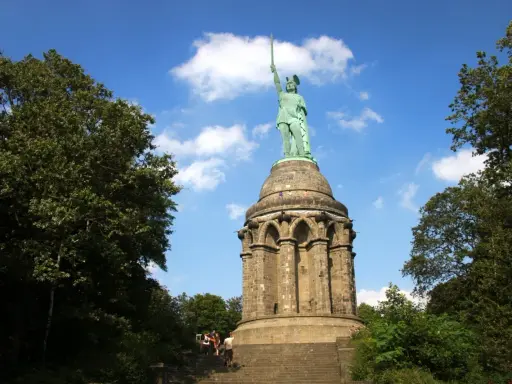 Aufstieg zum Hermannsdenkmal: Wanderer erklimmen die Stufen zum imposanten Reiterstandbild unter blauem Himmel.