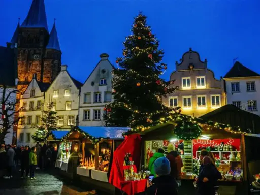 Festlicher Weihnachtsmarkt mit beleuchtetem Baum und Buden vor historischen Häusern. Ein Kandidat für den besten Weihnachtsmarkt NRW.