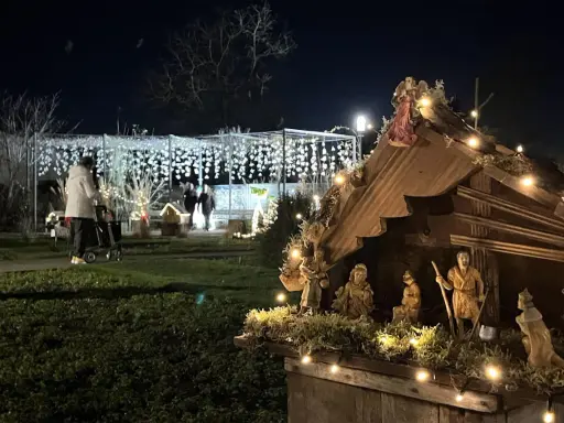 Bethlehemskrippe mit Figuren und Lichtern auf dem weihnachtsmarkt legden. Im Hintergrund eine Person mit Rollator und Lichterketten.