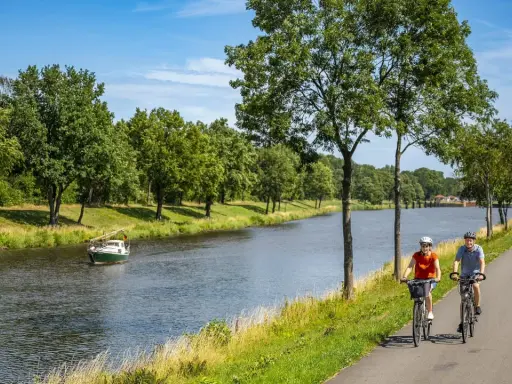 Zwei Radfahrer genießen eine Tour auf dem Dortmund-Ems-Kanal-Radweg. Ein kleines Boot fährt auf dem Wasser.