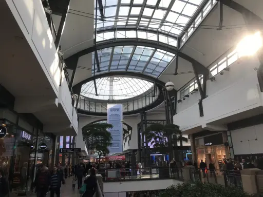 Helles, modernes Einkaufszentrum mit Glasdach. Menschen schlendern durch das Oberhausen Centro, vorbei an Geschäften wie Lacoste.