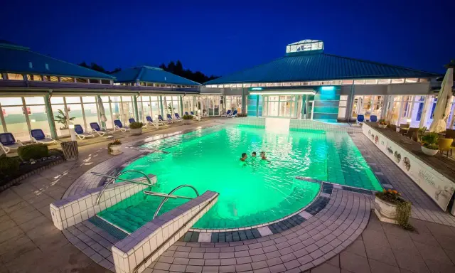 Abendliche Erfrischung im beleuchteten Pool der Therme Bad Driburg. Drei Personen genießen das warme Wasser unter dem klaren Nachthimmel.