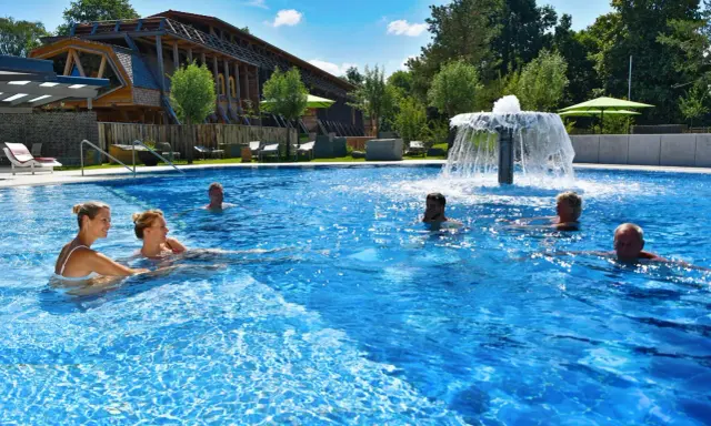 Entspannte Menschen genießen das Schwimmbad eines Kurortes in NRW. Ein Wasserspiel sorgt für Erfrischung.