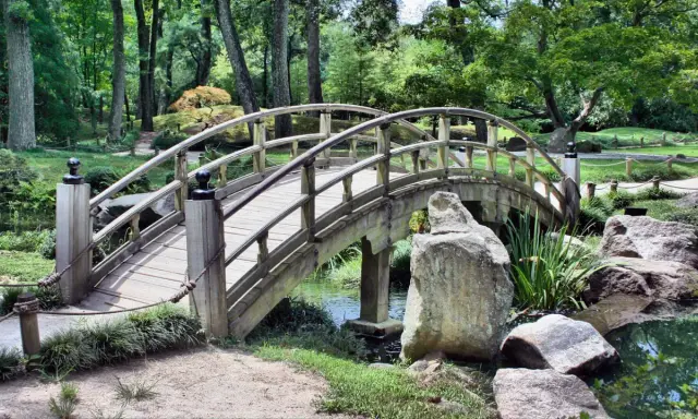 Eine hölzerne Bogenbrücke führt durch den grünen Herford Park. Ein kleiner Bach plätschert unter der Brücke hindurch.