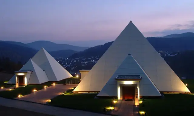 Zwei moderne Pyramiden im Sauerland, beleuchtet im Abendlicht, mit einem Dorf im Hintergrund.