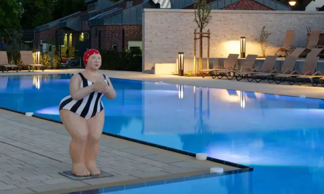 Skulptur einer Schwimmerin am beleuchteten Pool des Solebads Werne. Liegestühle und Bäume säumen das Becken.