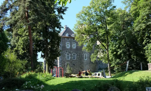 Ein sonniger Tag im Frankenberger Park. Kinder spielen auf einem Spielplatz vor einem alten Gemäuer, umgeben von üppigem Grün.
