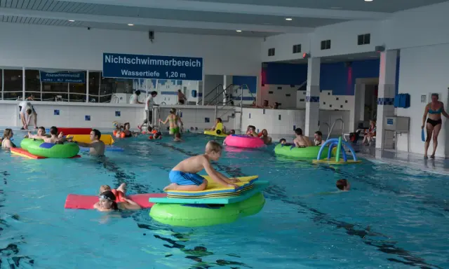 Kinder und Erwachsene planschen im Nichtschwimmerbereich des Schwimmbads Brakel. Viele nutzen bunte Schwimmtiere und Matten.
