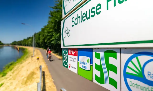 Radwegweiser am Schleusenweg zeigen den Verlauf des Emsland-Radwegs. Radfahrer genießen die Fahrt entlang des Kanals.