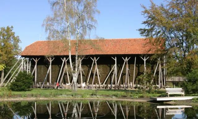 Große Gradierwerke mit roten Ziegeldächern, umgeben von Bäumen und einem Teich. Hier wird die Luft mit gesundem **saline rheine** angereichert.