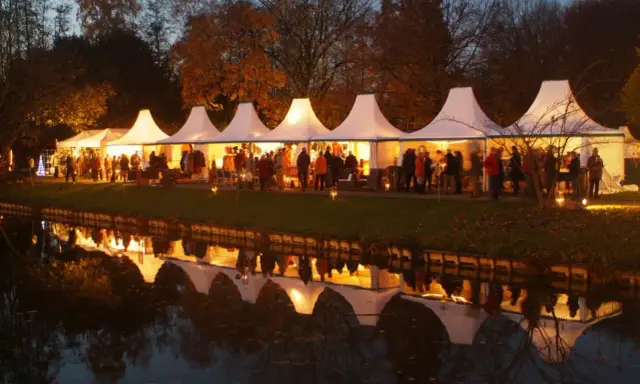 Festliche Zelte am havixbeck weihnachtsmarkt spiegeln sich im Wasser. Besucher bummeln durch die beleuchteten Stände.