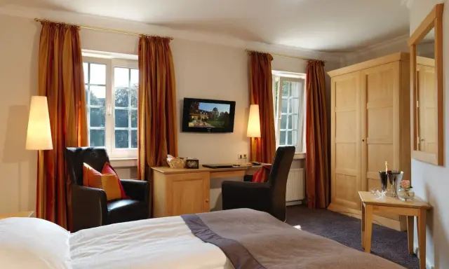 Gemütliches Zimmer mit Blick auf die Klosterpforte Harsewinkel. Einladende Sessel, Schreibtisch und ein großes Bett.