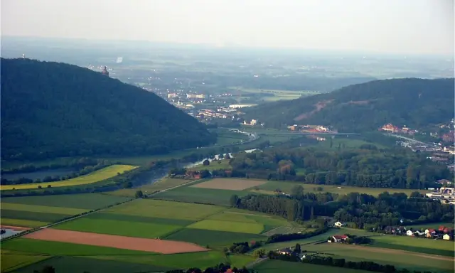 Blick über das Wesertal bei Porta Westfalica mit bewaldeten Hügeln, Feldern und der Stadt.