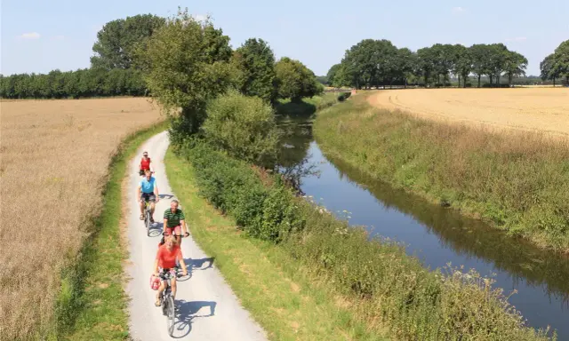 Radfahrer genießen die Fahrt auf dem werse ems radweg entlang eines Kanals und durch Felder.