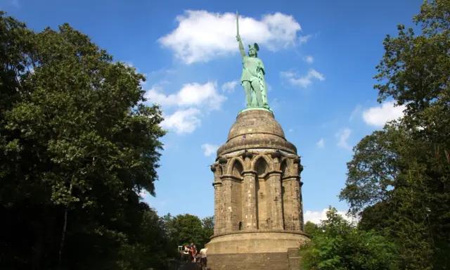 Aufstieg zum Hermannsdenkmal: Wanderer erklimmen die Stufen zum imposanten Reiterstandbild unter blauem Himmel.