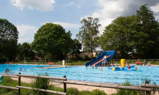Ein sonniger Tag im Freibad Lahde. Kinder planschen im Wasser, rutschen und spielen auf einem aufblasbaren Spielzeug.