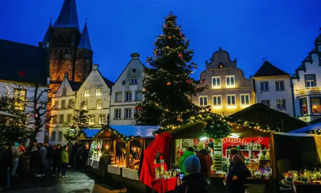 Festlicher Weihnachtsmarkt mit beleuchtetem Baum und Buden vor historischen Häusern. Ein Kandidat für den besten Weihnachtsmarkt NRW.