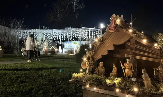 Bethlehemskrippe mit Figuren und Lichtern auf dem weihnachtsmarkt legden. Im Hintergrund eine Person mit Rollator und Lichterketten.
