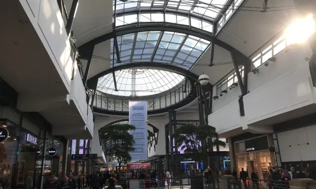 Helles, modernes Einkaufszentrum mit Glasdach. Menschen schlendern durch das Oberhausen Centro, vorbei an Geschäften wie Lacoste.