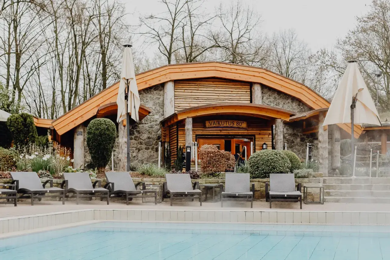 Entspannung am Pool des h2o Herford. Liegestühle laden zum Verweilen ein, während im Hintergrund die Sauna mit der Aufschrift "Vaikutus 80°" lockt.