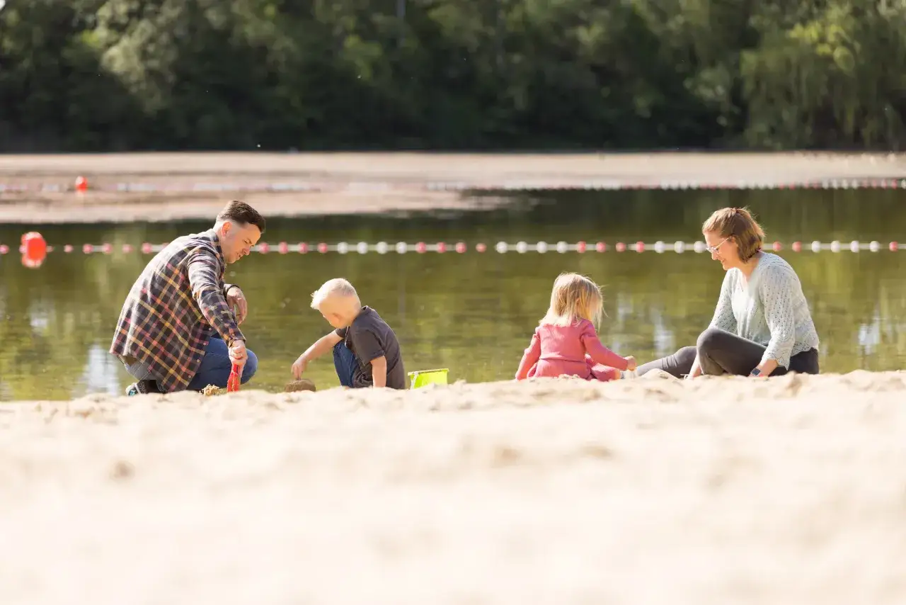 Familie spielt am Sandstrand des Badesee Mindenerwald. Vater hilft Sohn beim Sandburgen bauen, w&auml;hrend Mutter und Tochter daneben sitzen.
