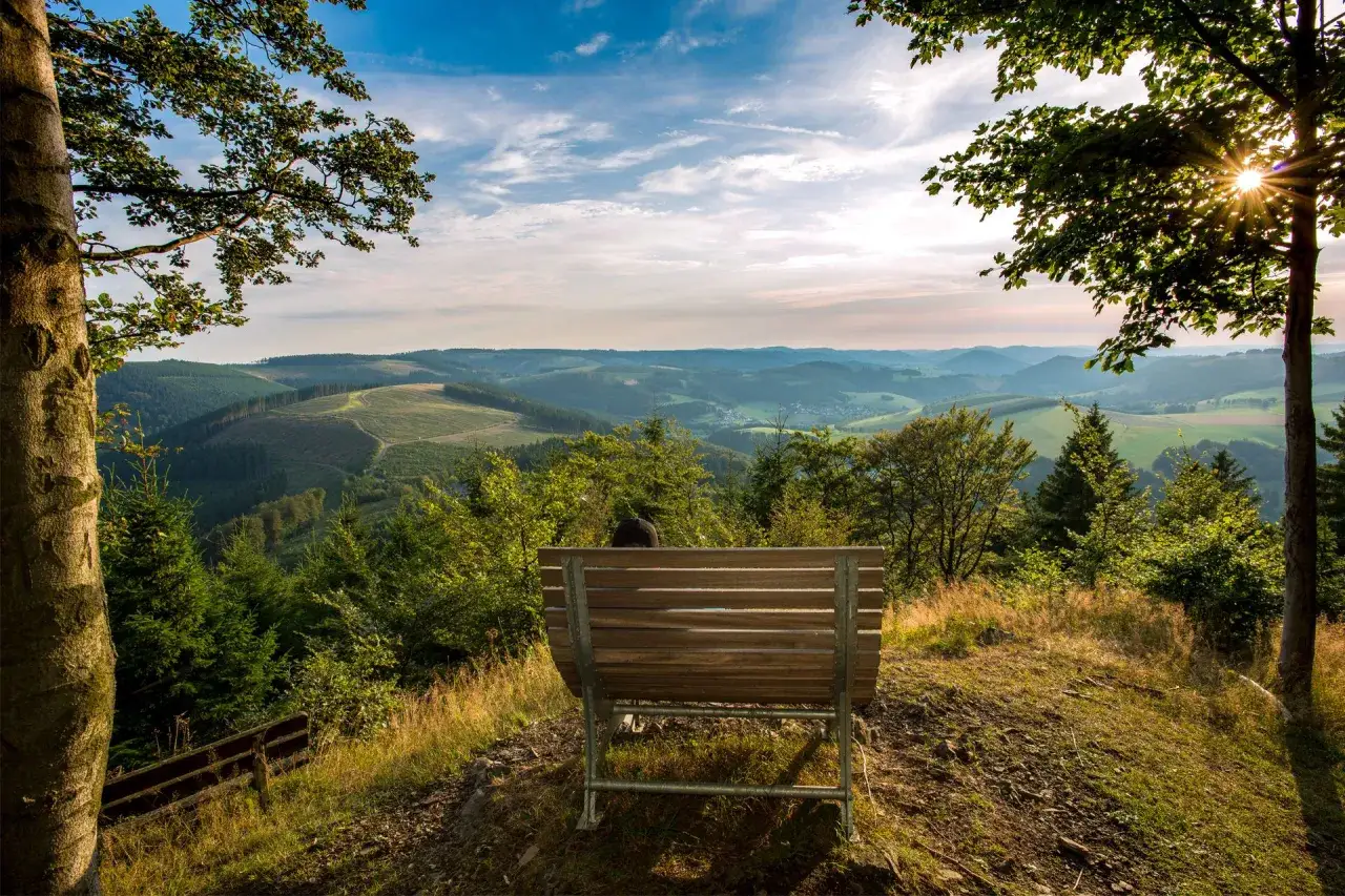 Ein Mensch sitzt auf einer Bank und blickt in eine weite Hügellandschaft. Ein Ort, der zum Innehalten einlädt, ein wahrer weg der sinne.