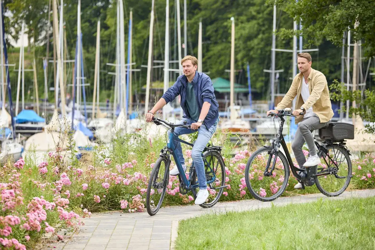 Zwei Männer genießen eine Fahrradtour in Haltern am See, vorbei an blühenden Rosen und Segelbooten.