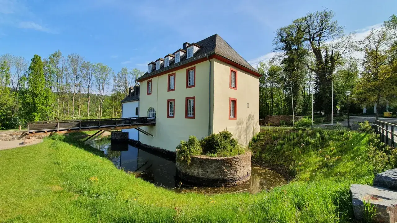Wasserschloss in Bad Laasphe, umgeben von einem Wassergraben und üppigem Grün. Eine Holzbrücke führt zum Eingang.