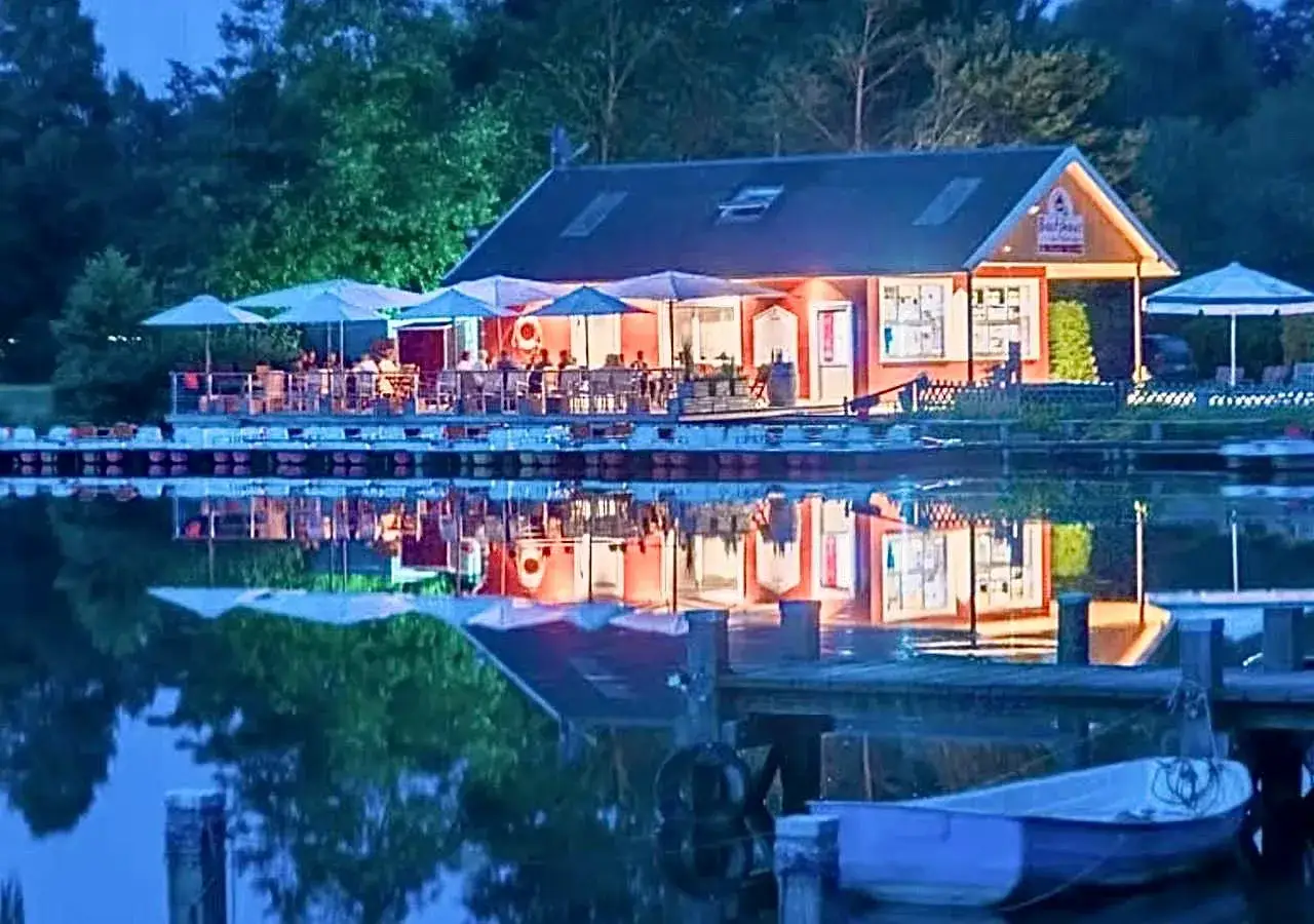 Abendstimmung am See in Borken. Ein Restaurant mit beleuchteter Terrasse und Sonnenschirmen spiegelt sich im ruhigen Wasser.