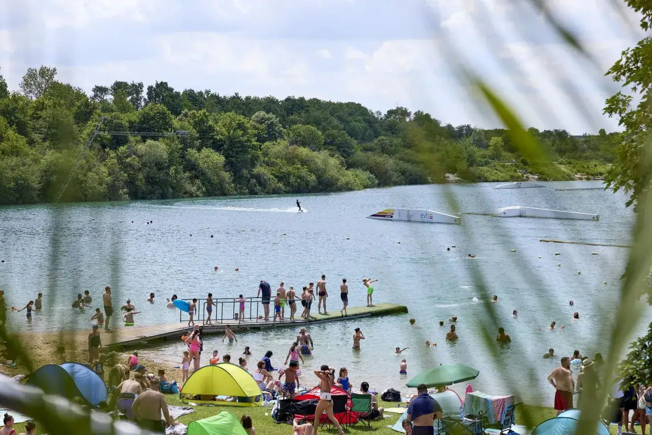 Menschen genie&szlig;en einen sonnigen Tag am Beckum See mit Wasserski und Entspannung am Ufer.
