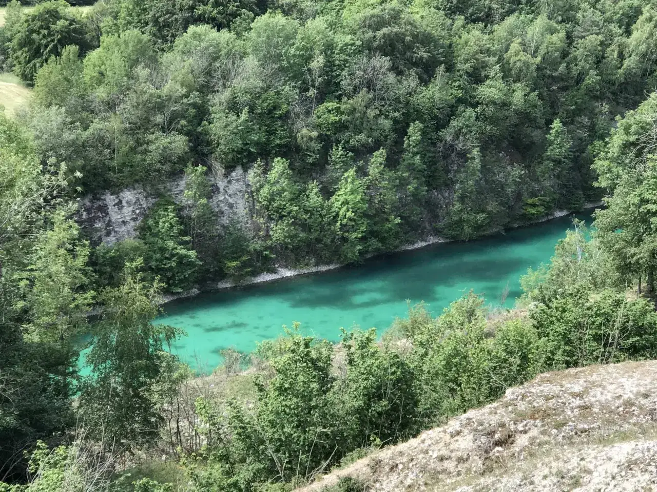 Eine malerische blaue Lagune im Teutoburger Wald, umgeben von üppigem Grün und Felsformationen.