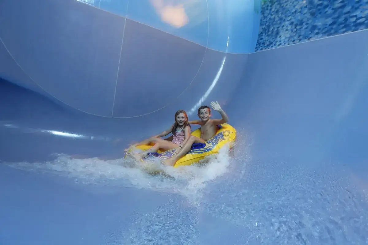 Zwei Kinder rutschen lachend auf einem gelben Reifen die Wasserrutsche im h2o herford hinunter.
