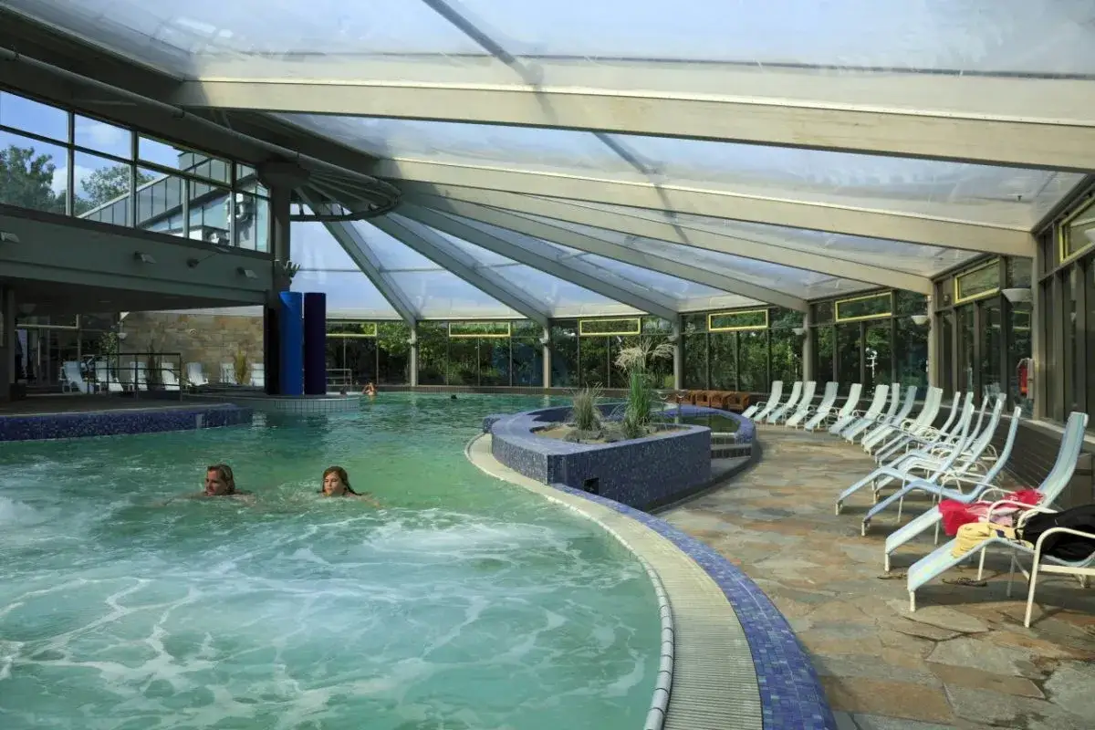 Zwei Frauen schwimmen im Mattlerbusch Schwimmbad unter einem transparenten Dach. Liegest&uuml;hle laden zum Entspannen ein.