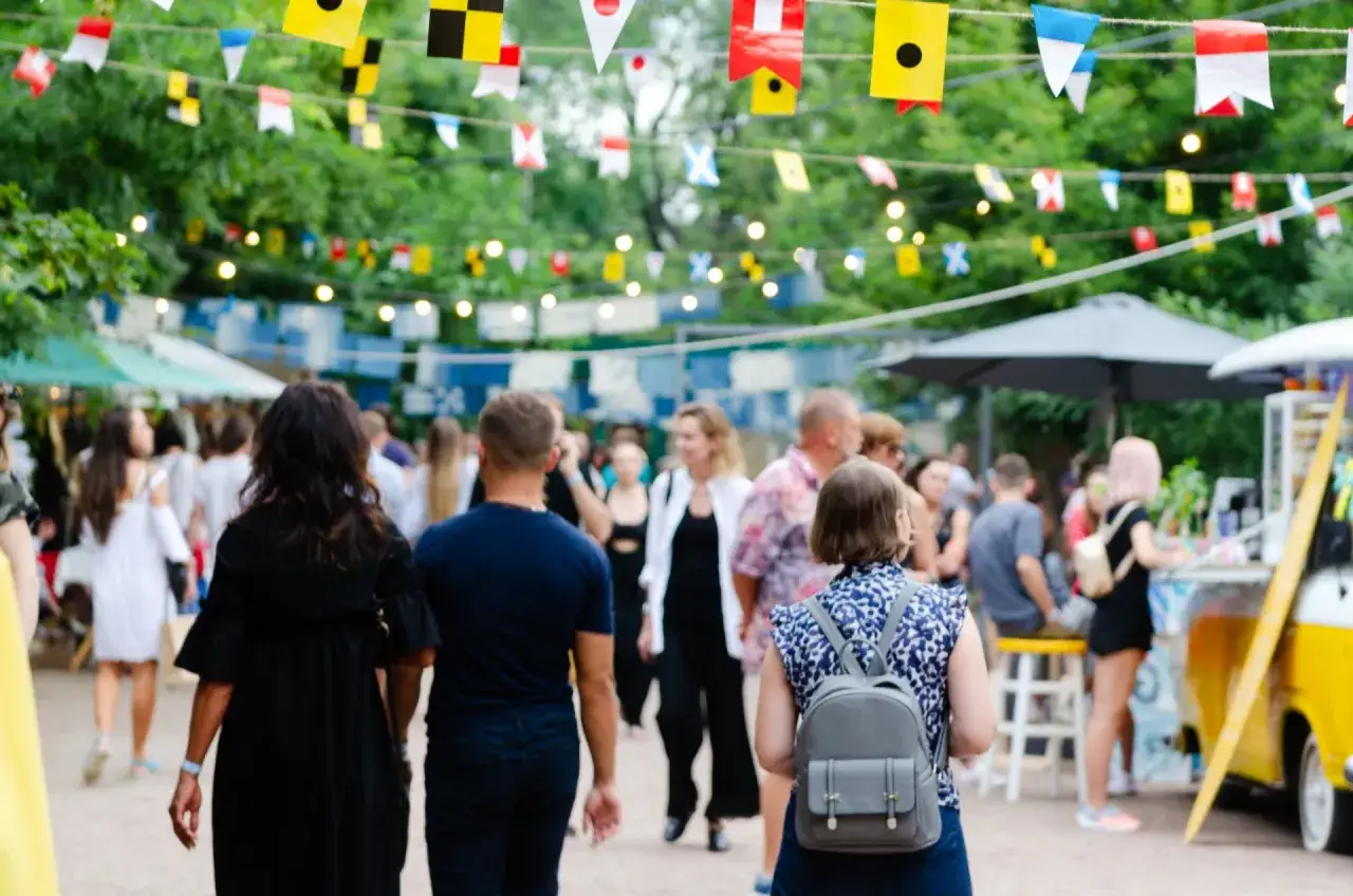 Bunte Flaggen schm&uuml;cken die Havixbeck Veranstaltungen. Menschen schlendern &uuml;ber einen belebten Markt mit St&auml;nden und Essen.