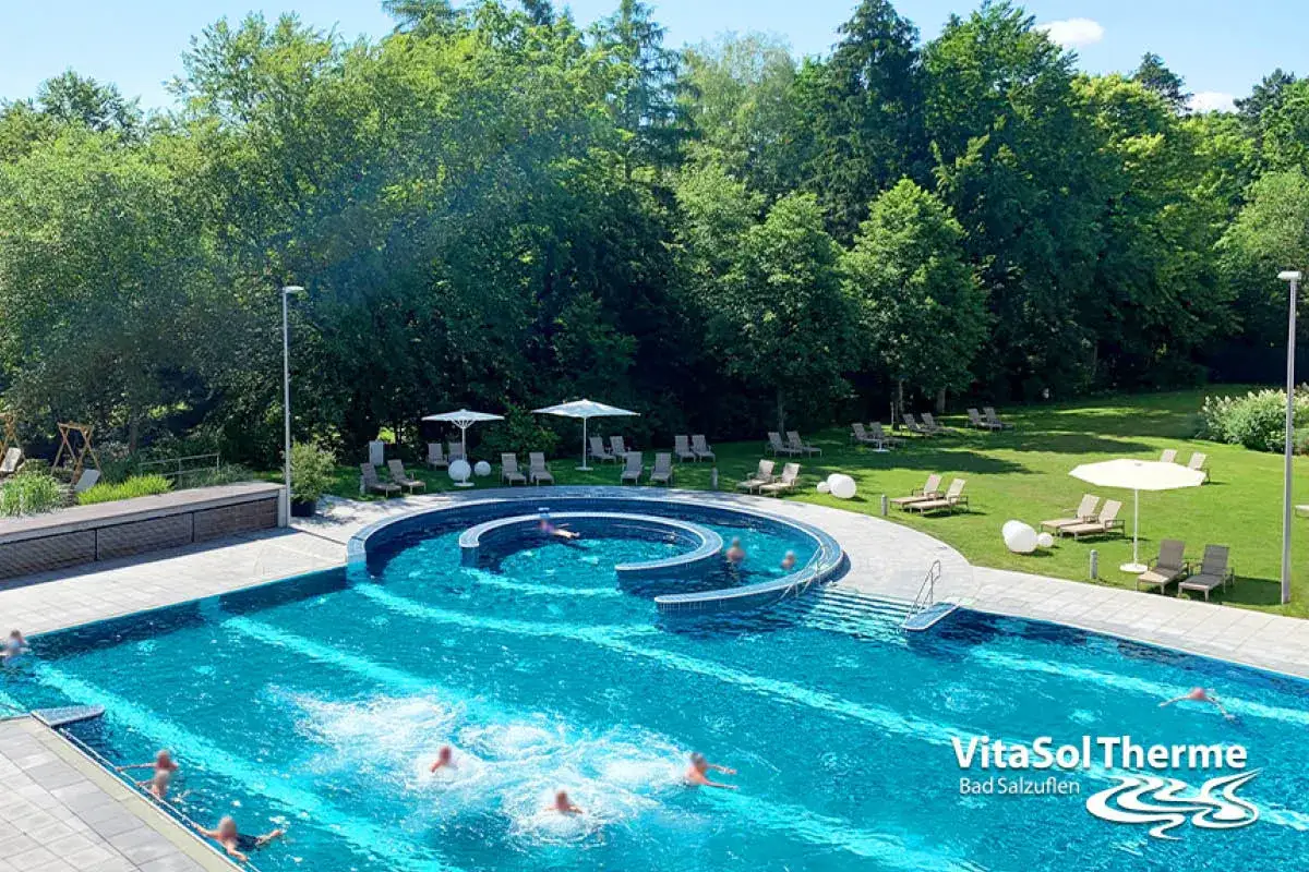 Erfrischendes Schwimmbad mit Liegewiese und Bäumen. Die VitaSol Therme Bad Salzuflen lädt zum Entspannen ein.