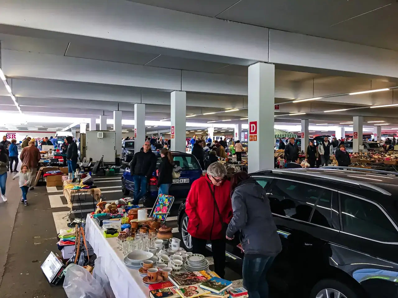 Buntes Treiben auf dem Flohmarkt Paderborn. Menschen stöbern an Tischen voller Geschirr, Kleidung und Kuriositäten. Autos dienen als Verkaufsstände.