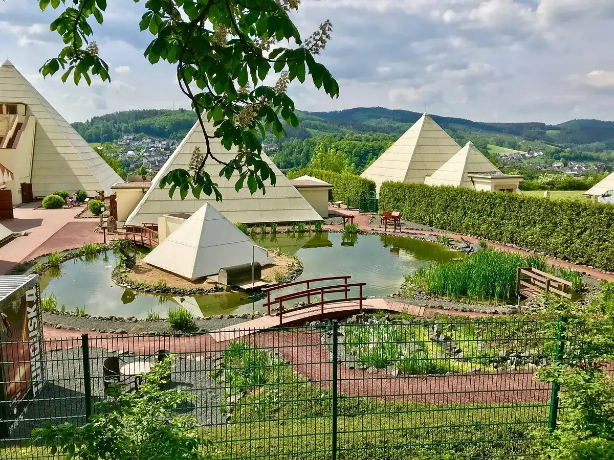 Die Sauerland-Pyramiden, ein Teich mit Br&uuml;cken und &uuml;ppige Vegetation unter einem bew&ouml;lkten Himmel.