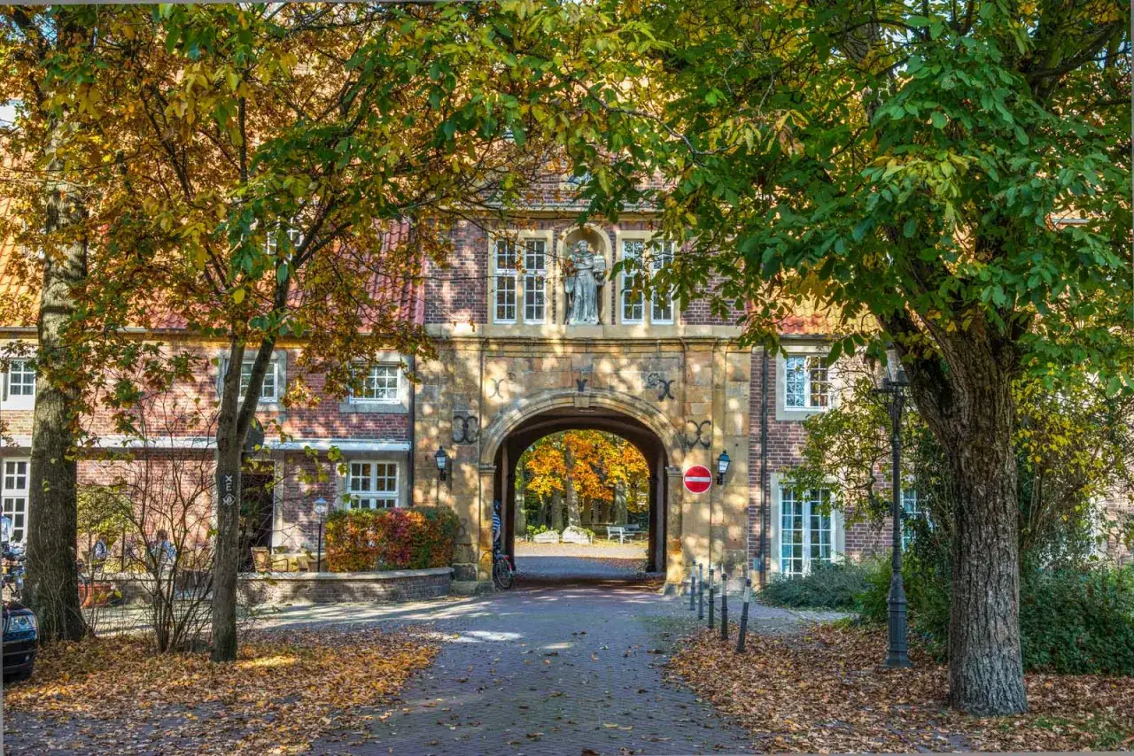 Herbstliche Farben schm&uuml;cken die Klosterpforte Harsewinkel. Ein Torbogen f&uuml;hrt zu einem Hof mit bunten B&auml;umen.