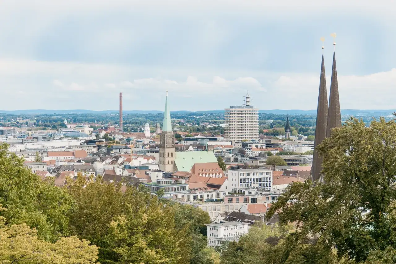 Ein Tag in Bielefeld: Blick &uuml;ber die Stadt mit Kircht&uuml;rmen, einem Hochhaus und einem alten Schornstein.