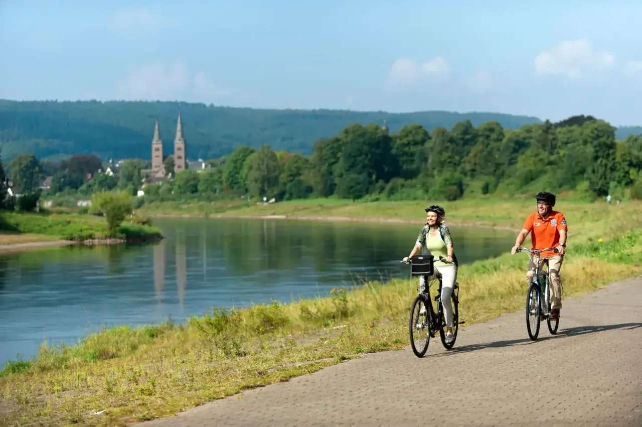 Ein Paar genießt sein Fahrrad Wochenende am Fluss. Im Hintergrund eine Stadt mit Kirchtürmen und grüne Hügel.
