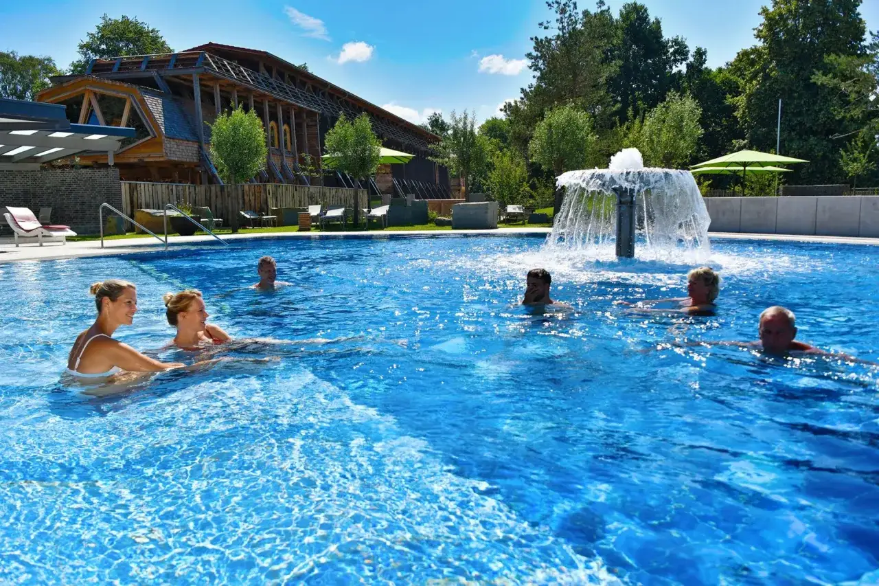 Entspannte Menschen genie&szlig;en das Schwimmbad eines Kurortes in NRW. Ein Brunnen sprudelt im Hintergrund.