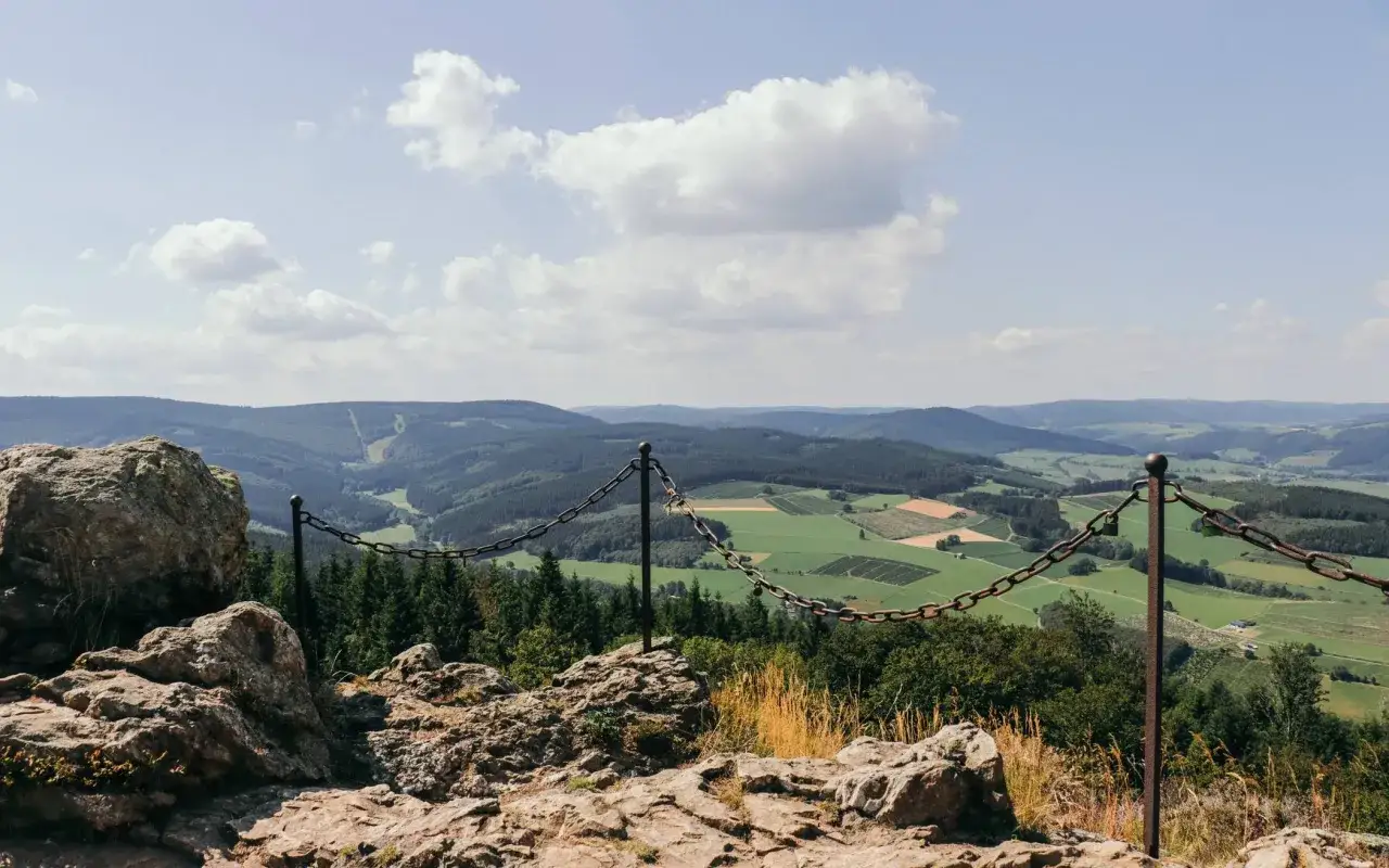 Felsiger Aussichtspunkt mit Kettenabsperrung und Blick über grüne Täler und Wälder. Perfekt für eine Wanderung in NRW.