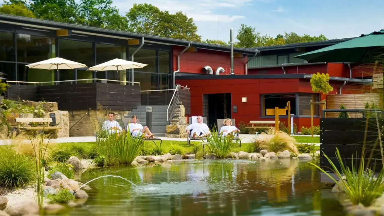 Entspannte Gäste in weißen Roben ruhen sich am Teich der Olsberg Therme aus.